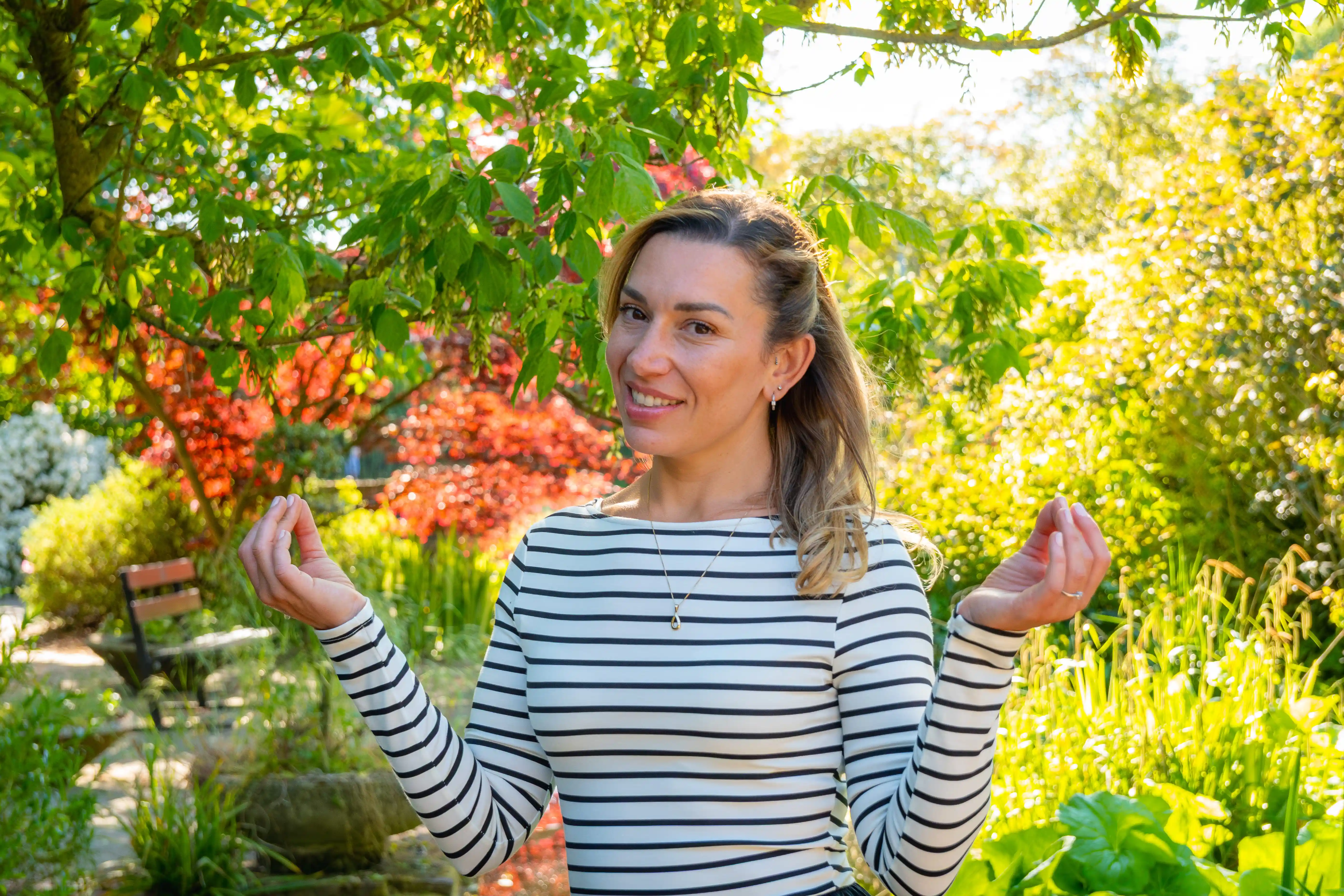 A female coach meditating in a luscious, colourful garden